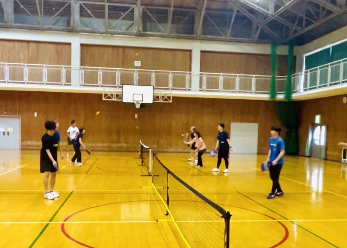 体育館でネットを挟んでピックルボールを楽しむ参加者